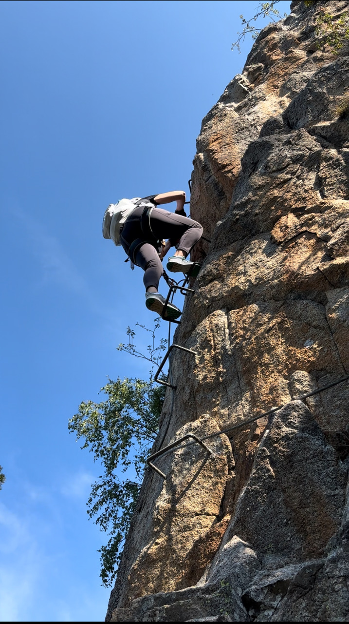 Climbing a steep rock face with via ferrata equipment in Andorra