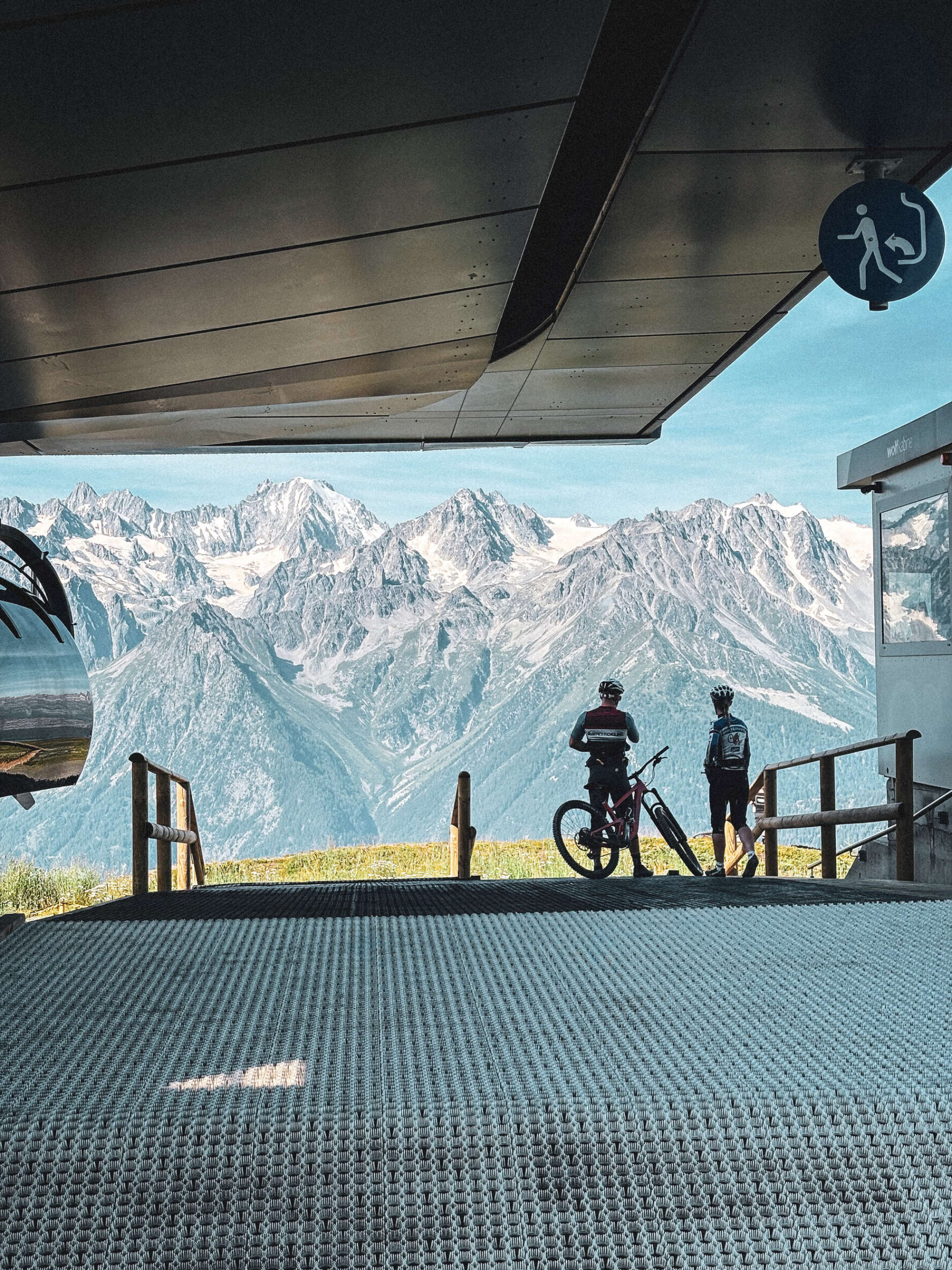 Cyclists at a lift station overlooking Alpine peaks