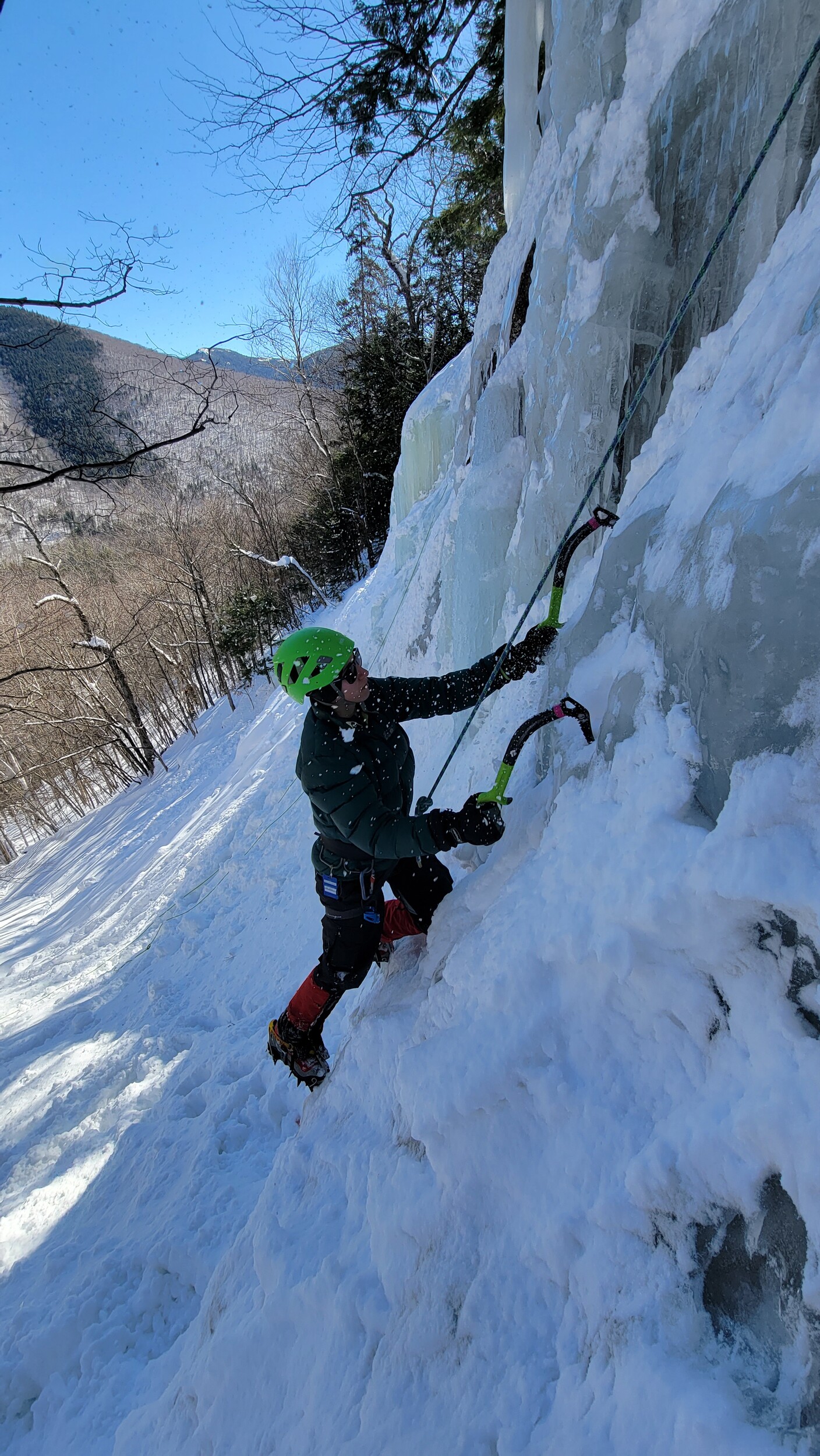 Ice climber on a frozen waterfall in New Hampshire with trees in the background