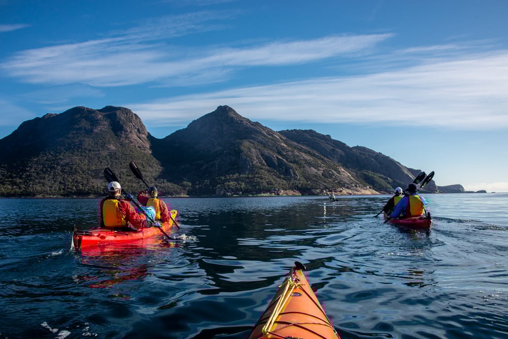 Kayakers on a calm sea with the peaks of Freycinet Peninsula in the background