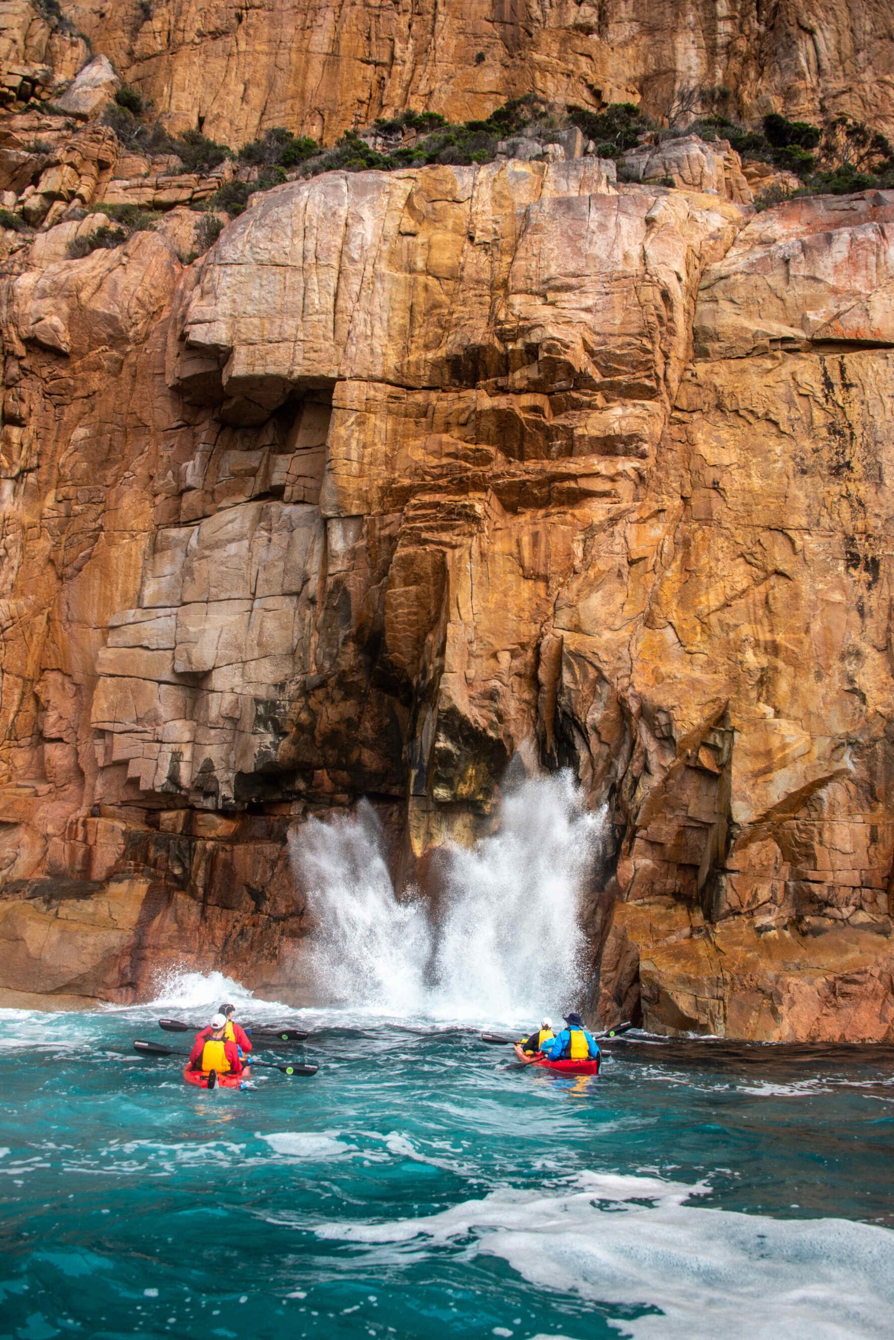 Kayakers on waves near a vibrant rocky cliff