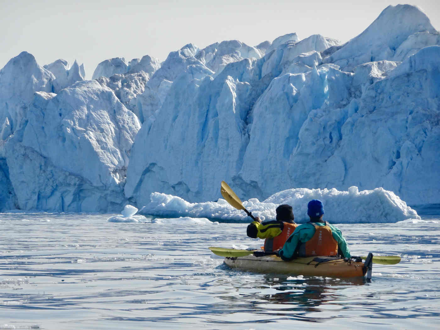 Two people kayaking near a large glacier on a calm sea