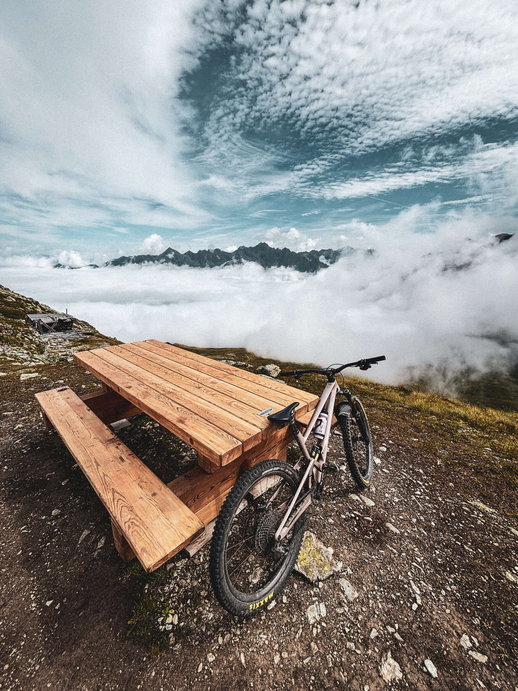 MTB resting against a wooden bench above the clouds in the Alps