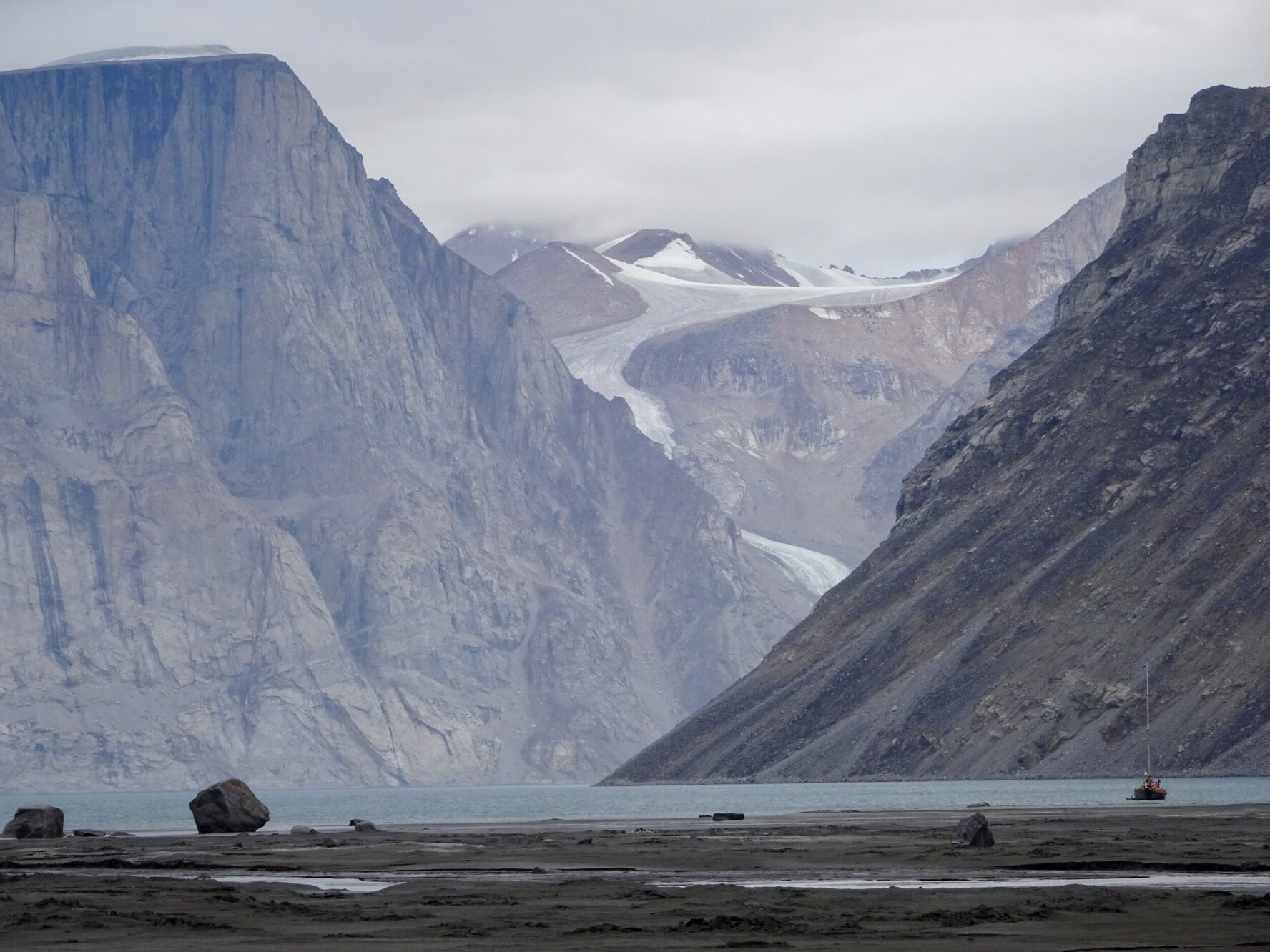 Glacial fjord with steep cliffs and a sailboat on the water