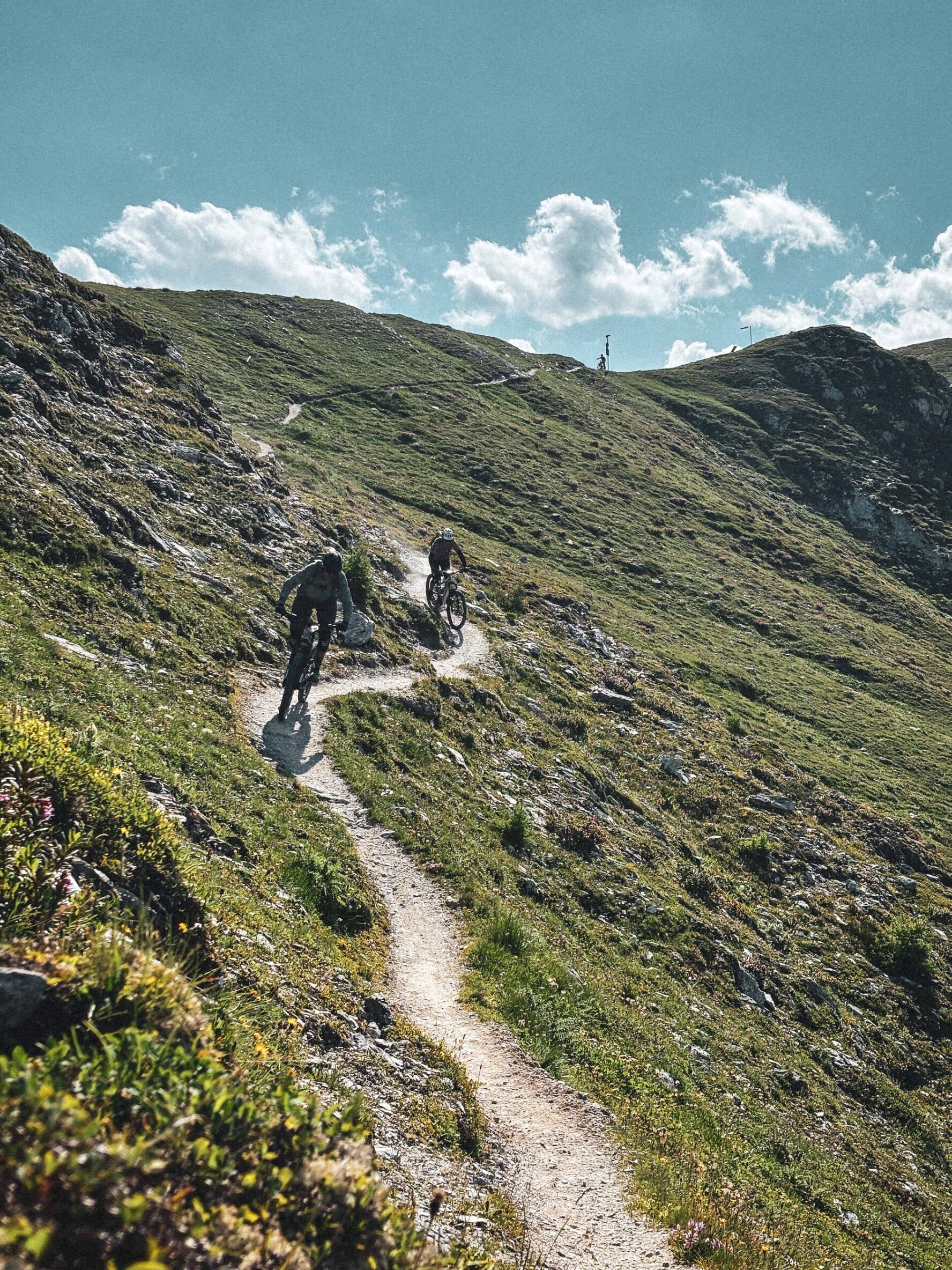 Two cyclists on a mountain trail in Valais with green slopes