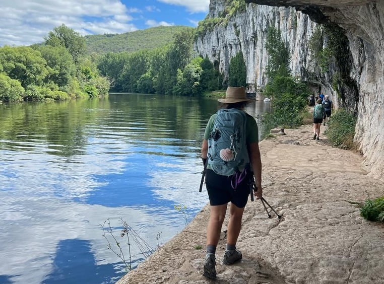Hiker on a path near a lake and under cliff formations in France