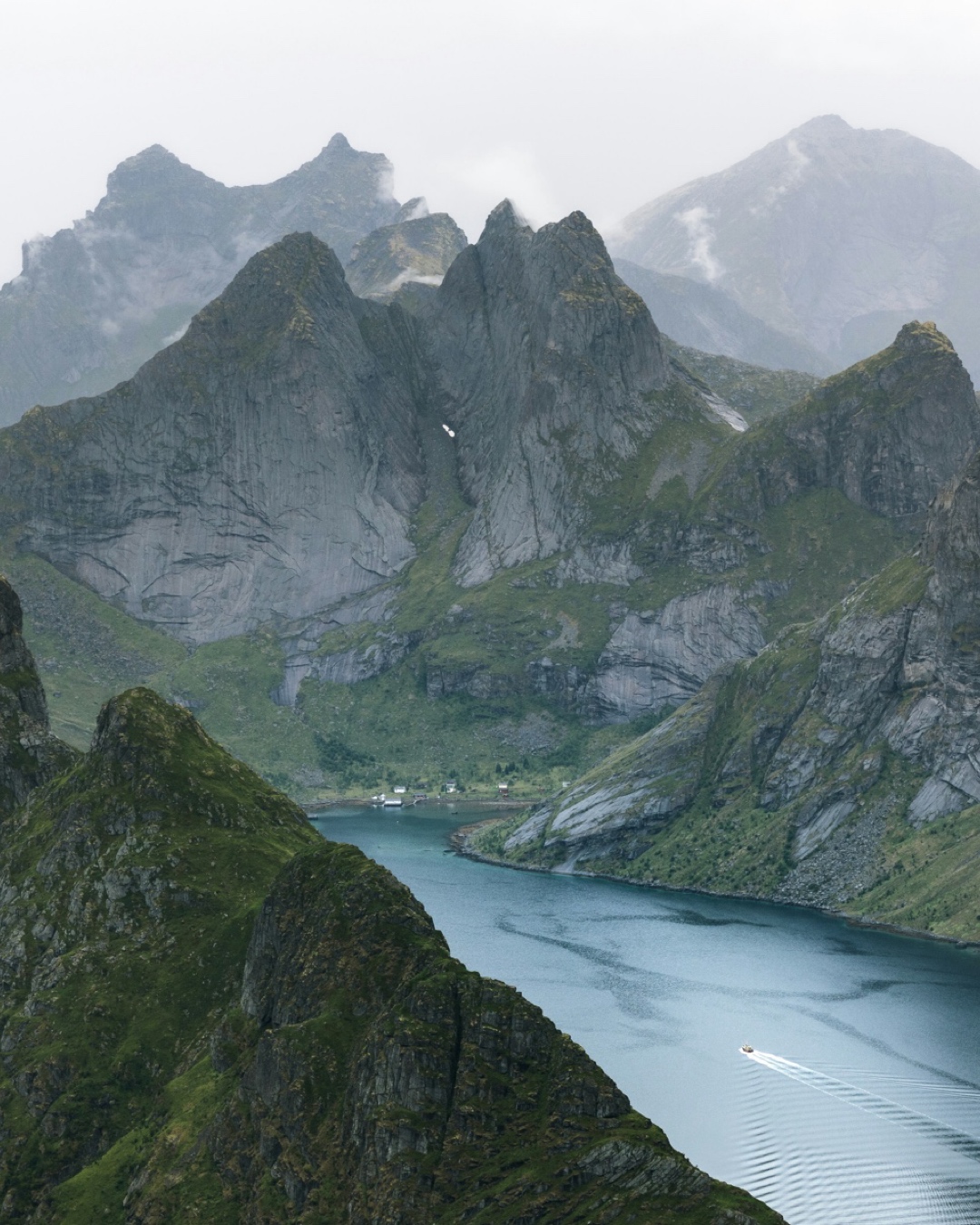 View from above of a boat in a fjord and tall mountains in Lofoten