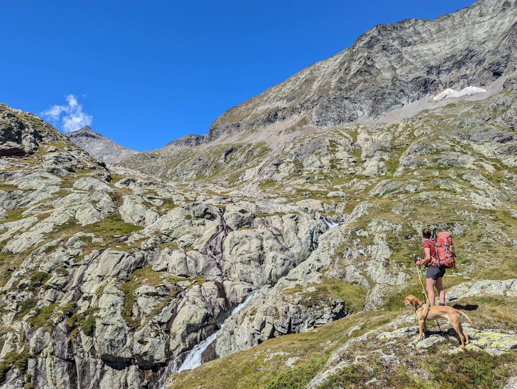A hiker and a dog underneath rock formations on the Glockner Trail