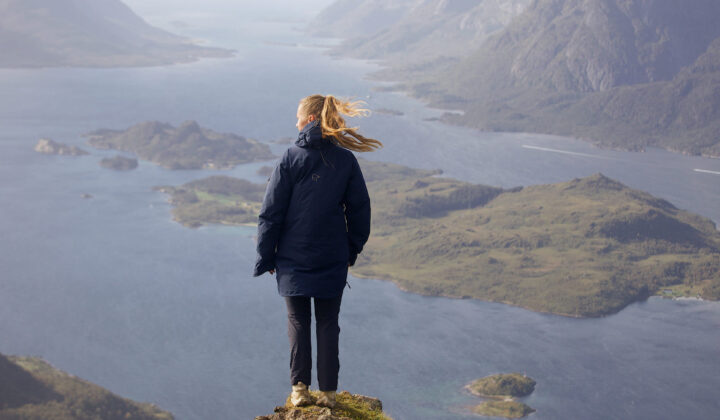Hiker on a viewpoint facing a fjord and panoramic view of Lofoten