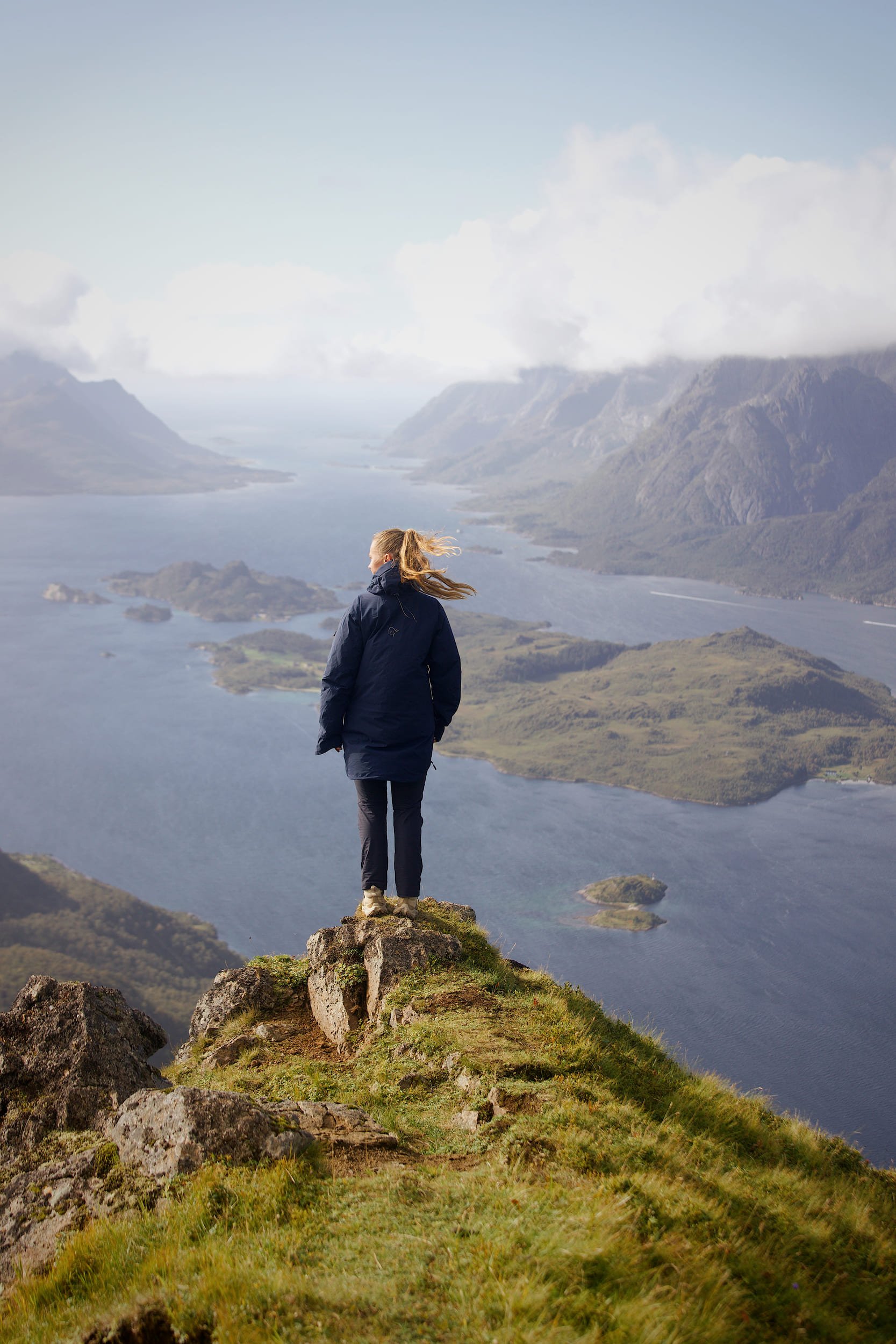 Hiker on a viewpoint facing a fjord and panoramic view of Lofoten
