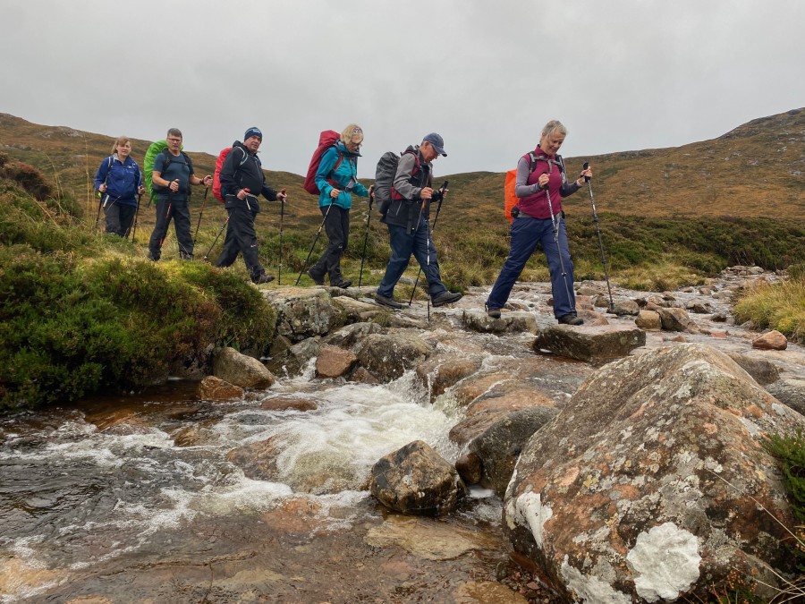 Hikers crossing a stream on the West Highland Way tour in Scotland
