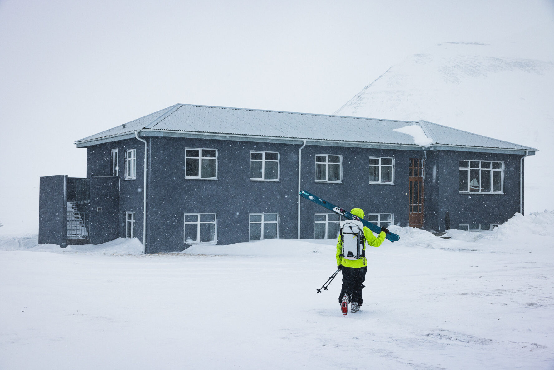 Skier carrying his skis to Soti Lodge after backcountry skiing, North Iceland