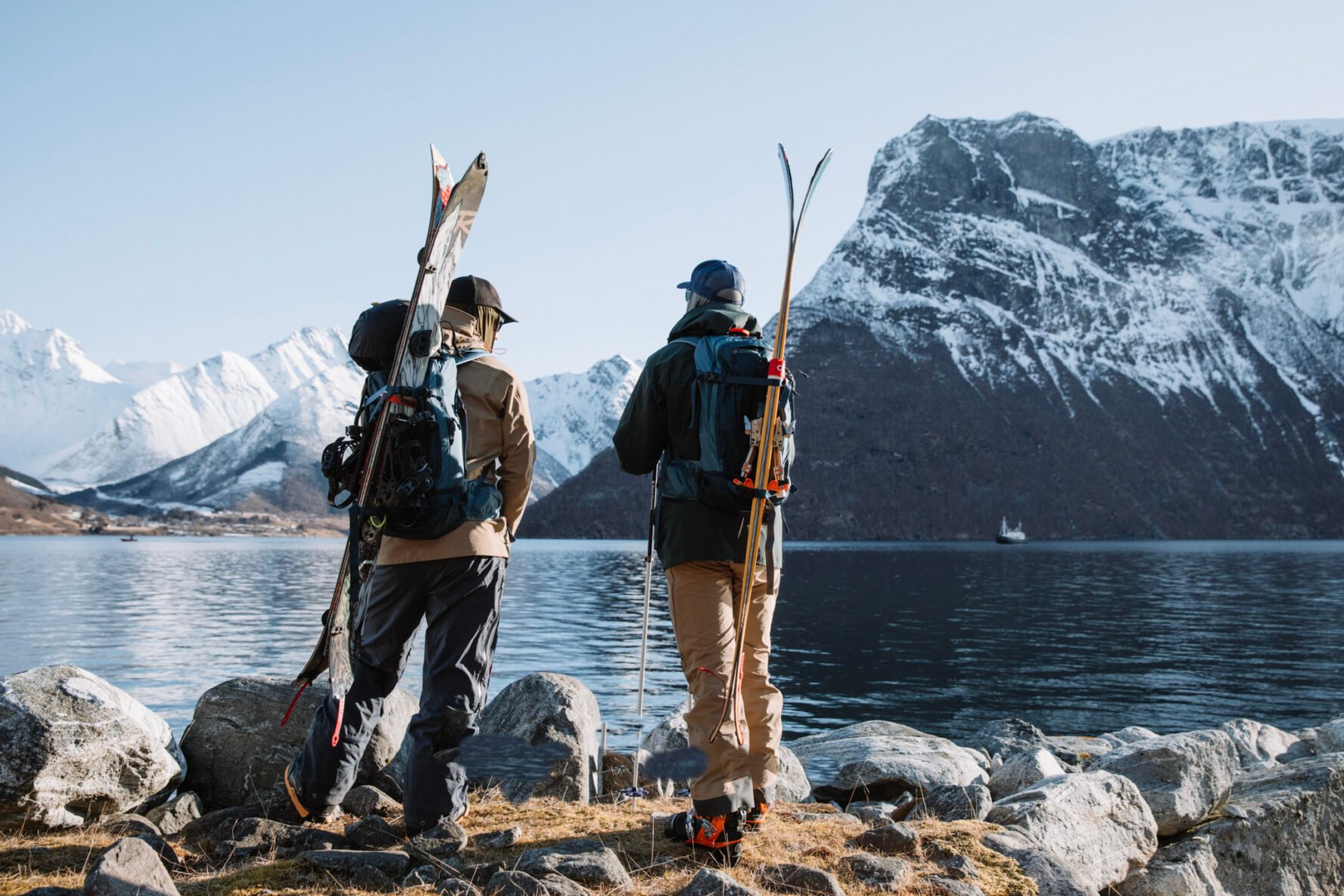 Two skiers near shore looking at a snowy landscape in Lofoten