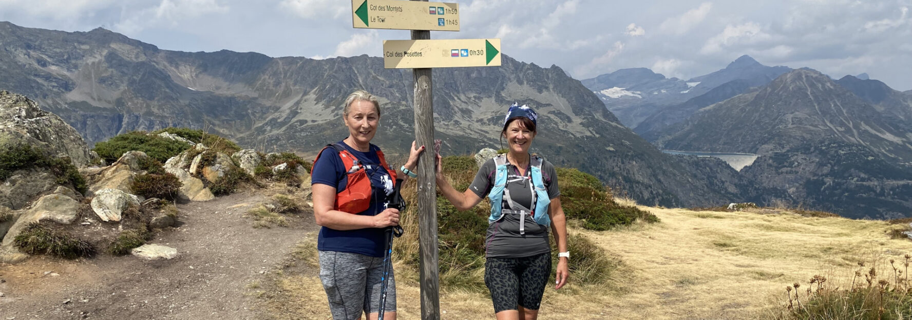 Two trail runners next to a signpost pointing to Col des Posettes in the Alps