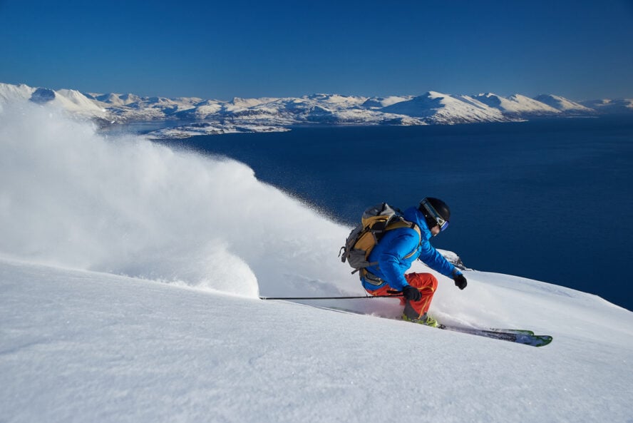 Skier spraying powder snow with the fjord and the snow covered mountains in the background.