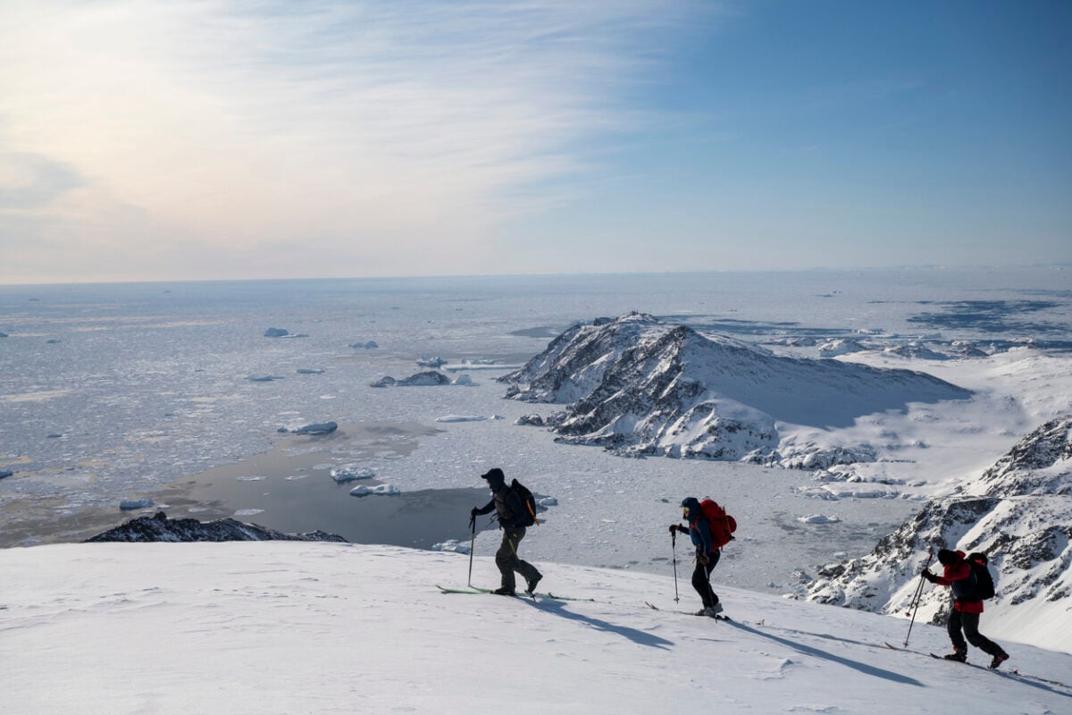 Distant view of ski mountaineers ascending snowcapped mountain across glacial plain in Greenland