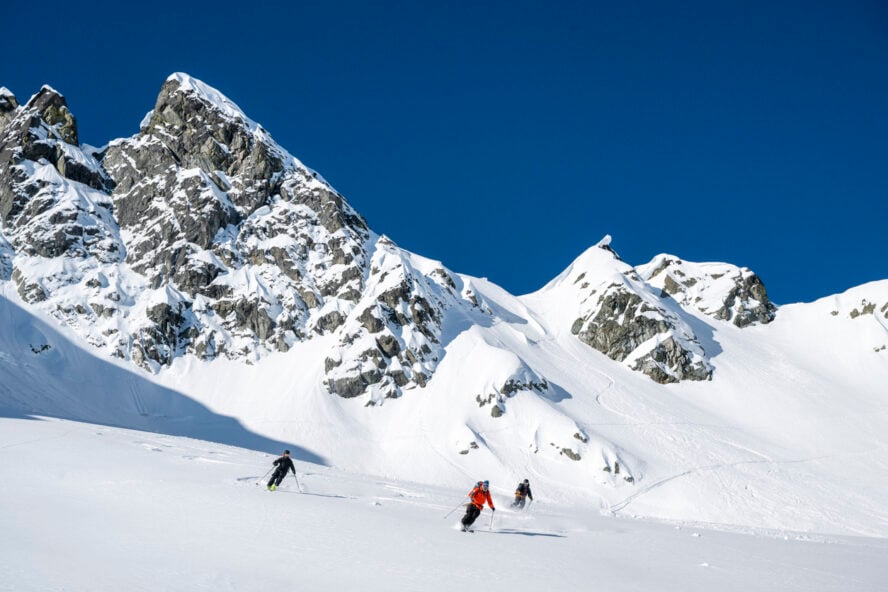 Group of beginner backcountry skiers descend high mountain slope through fresh powder snow