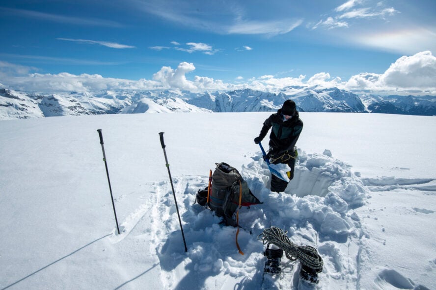 Skier digging a snow pit on top of a mountain - backcountry skiing for beginners advice