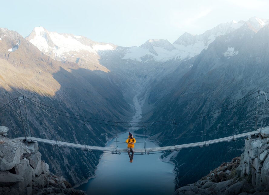 Man in yellow jacket sitting on a suspension bridge over a lake in Olpererhutte, Austria