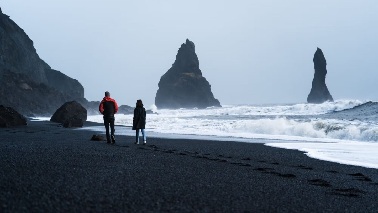 Two people walking black beach