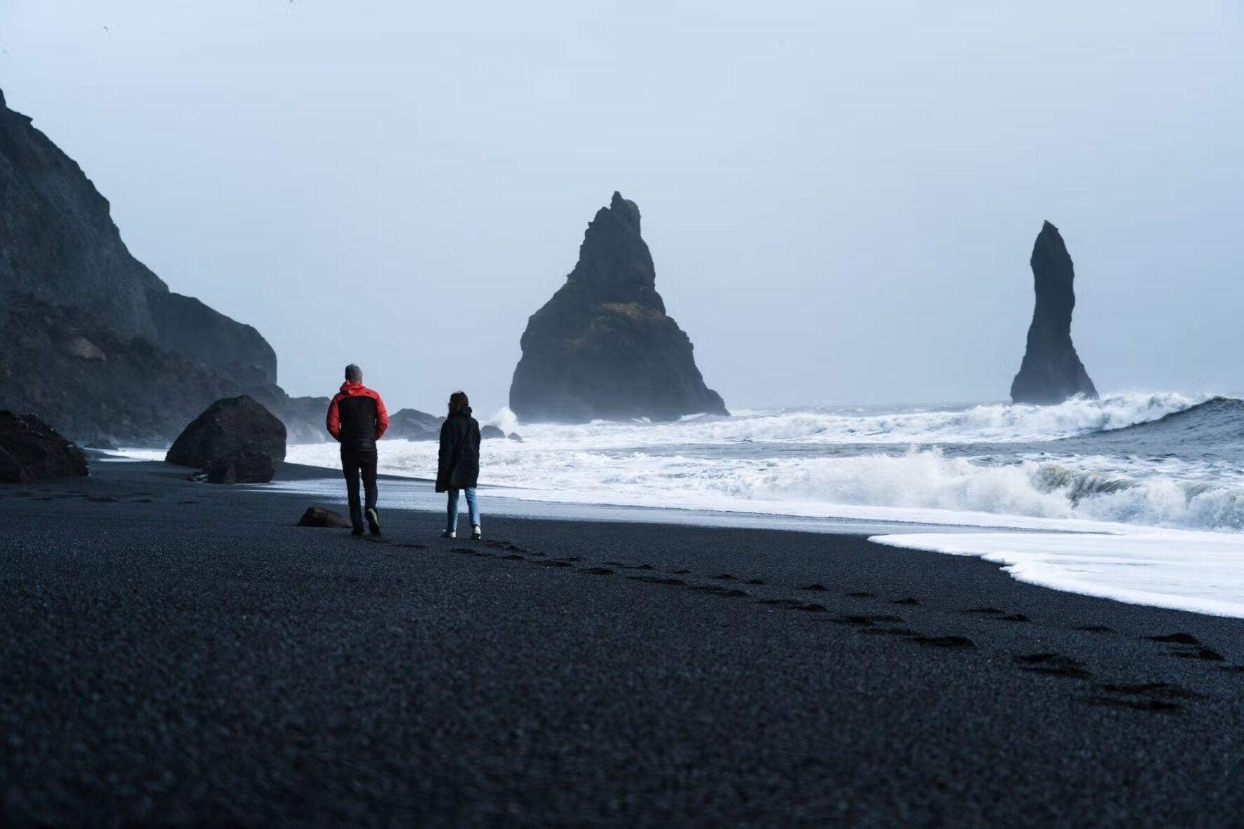 Two people walking black beach