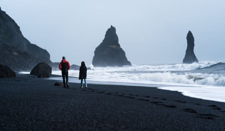 Two people walking black beach