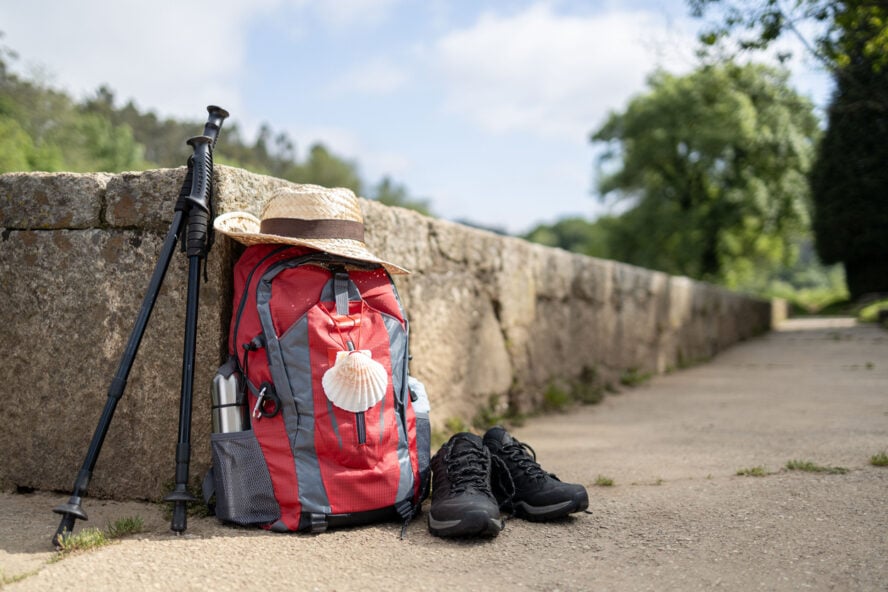 A backpack, hiking boots, trekking poles, and a hat rest against a stone wall, ready for an outdoor adventure along the Camino Portuguese Coastal Route