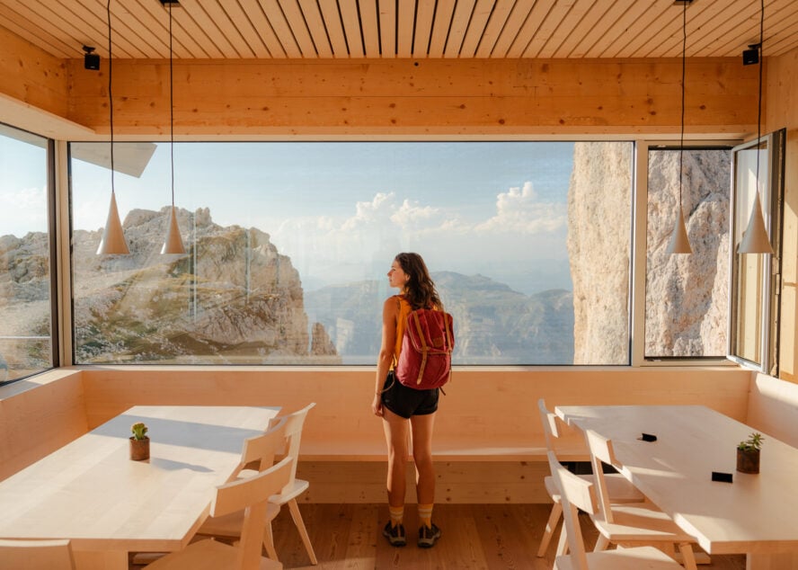 Serene woman looking through the window in alpine shelter at the view of Dolomites