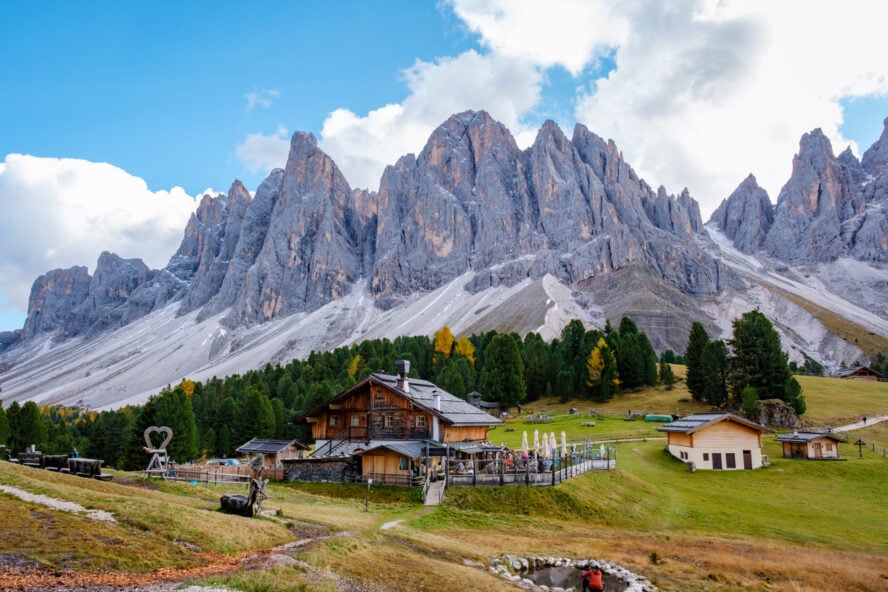 Breathtaking peaks of the Dolomites rise dramatically above charming wooden chalets nestled in lush green meadows, Geisleralm Dolomites Val Di Funes in Italy