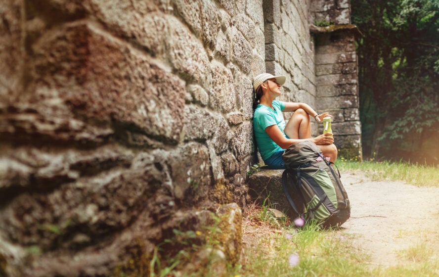 Tired female backpacker resting on the bench near the old antique brick wall castle on the famous Camino de Santiago 