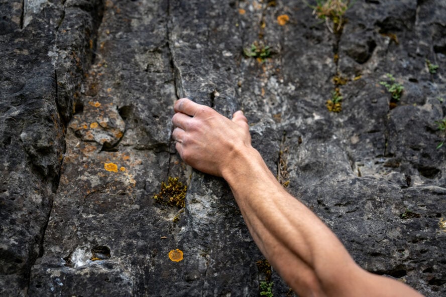 Close-Up Of Pinch Hold During Sport Climbing: Chalked Hand Gripping Rough Limestone Rock Surface With Precision And Strength In Outdoor Climbing Area In Bavaria, Germany