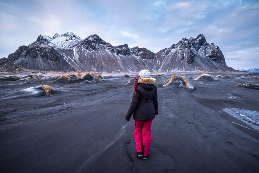 woman exploring Stokksnes with Vestrahorn mountain in the background at sunset in winter