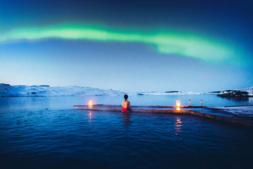 Young woman enjoying the scenic view of the Northern Lights above the lake and pool in Iceland