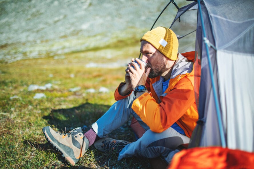An adult man drinking coffee in his hiking boots