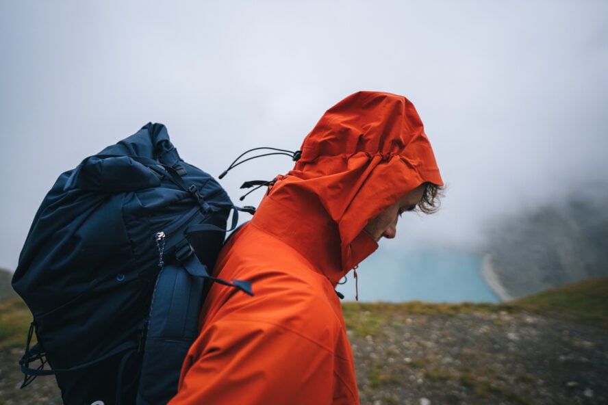 Backpacker explores alpine meadow above lake on moody day, Nufenen Pass, Valais/Ticino Cantons, in a jacket choosing what to wear for hiking