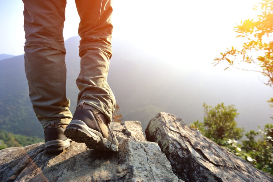 A hiker and his feet in hiking boots in front of a huge mountain vista in the USA