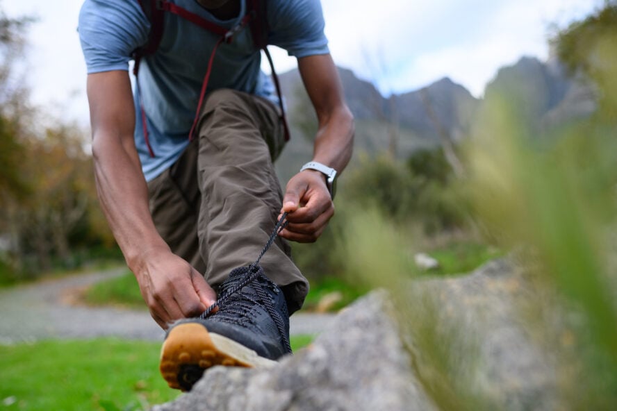 Solo hiker tying boot laces in preparation for journey amidst scenic landscape