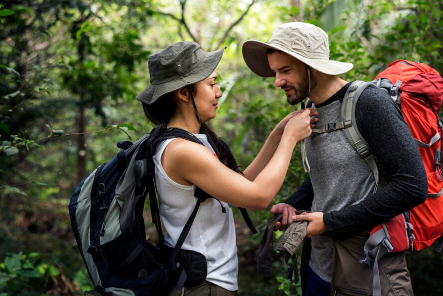Hikers trekking in a forest fixing their hat, one of the things from the list of what to wear hiking