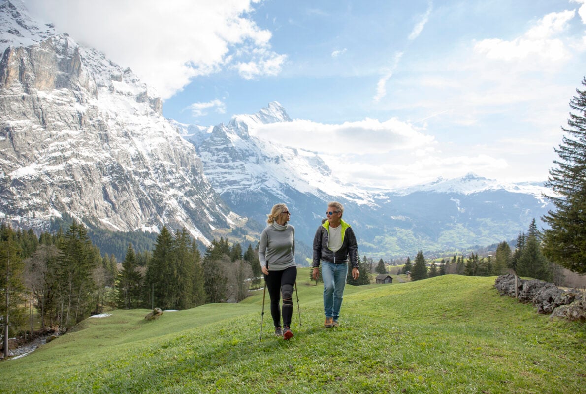 Hiking couple walk through grassy meadow in spring