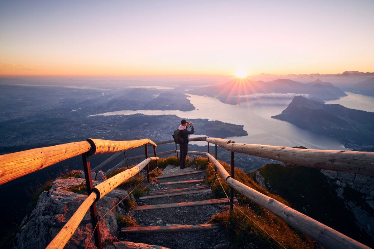 Man photographing landscape with lake and mountains at beautiful sunrise. View from Mount Pilatus, Lucerne, Switzerland, on one of the best hikes there