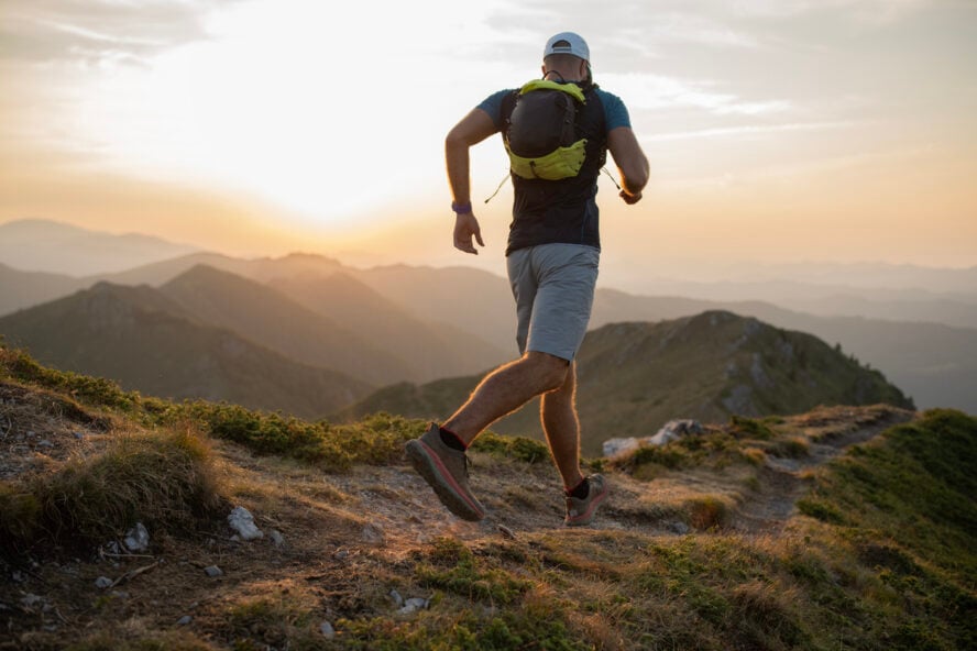 Male runner is jogging on the ridge of a mountain in hiking shorts at sunset