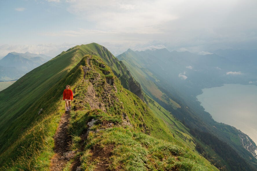 Woman in red coat hiking in Swiss Alps above Brienz lake in summer. Augstmatthorn