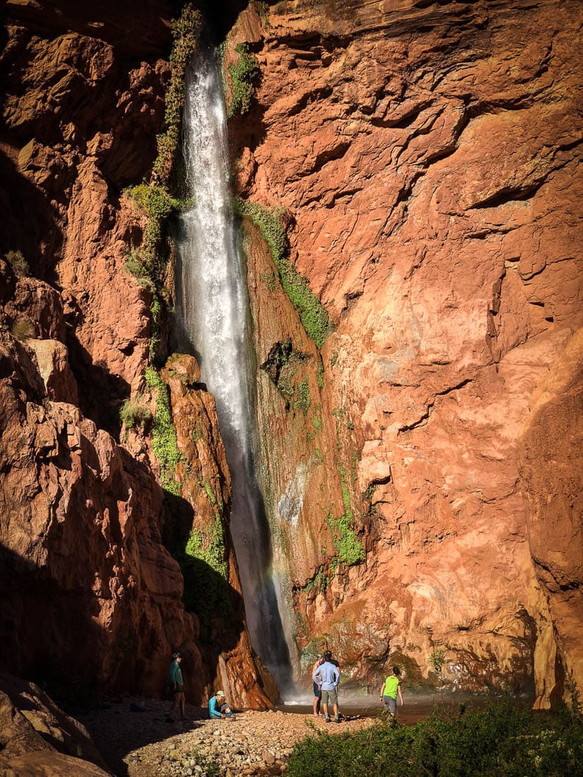 hikers beneath canyon waterfall