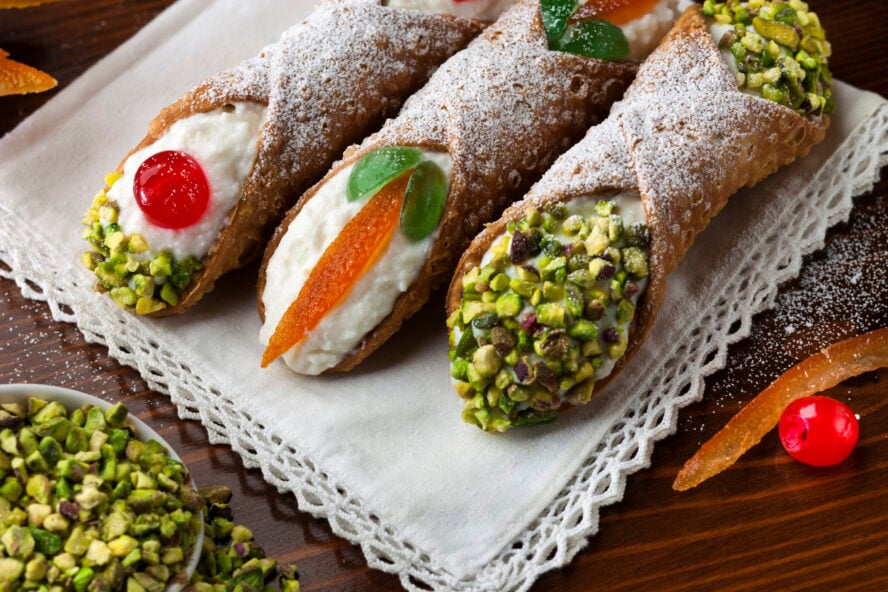 Three sicilian cannoli with ingradients on wooden table