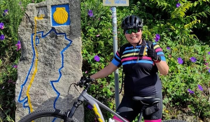 Image 7: Cyclist beside a Camino waymarker surrounded by green foliage