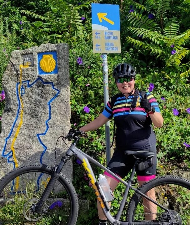 Image 7: Cyclist beside a Camino waymarker surrounded by green foliage